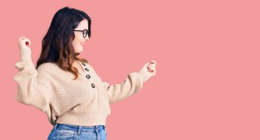 Güzel, genç, esmer, gündelik kıyafetler giymiş, gözlüklü, mutlu ve neşeli dans eden, gülümseyen, rahat ve kendinden emin bir kadın. 