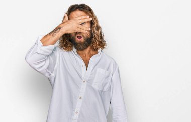 Sakallı, uzun saçlı, sıradan kıyafetler giyen, yüzü ve gözleri kapalı, utangaç ifadesiyle parmaklarının arasından bakan yakışıklı bir adam.. 