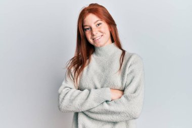 Kış süveteri giyen, kollarını kavuşturup kameraya gülümseyen genç kızıl saçlı kız. pozitif kişi. 