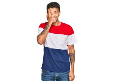 Genç, yakışıklı, Afro-Amerikalı bir adam günlük kıyafetler giyiyor. Bir gözünü eliyle kapatıyor. Yüzünde kendine güvenen bir gülümseme ve sürpriz bir duygu var.. 