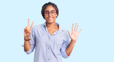 Saçları örgülü ve gözlüklü genç Afro-Amerikalı kadın yedi numarayı gösterip gösterirken kendinden emin ve mutlu gülümsüyor.. 