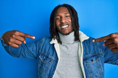 Saçları örgülü, normal kot ceketli, kendine güveni olan, kendini gururlu ve mutlu parmaklarıyla gösteren Afrikalı Amerikalı bir adam.. 