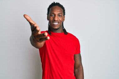 Saçları günlük kıyafetlerle örülü Afro-Amerikan bir adam gülümseyerek dostça el sıkışarak selamlama ve hoş geldin diyor. başarılı iş. 