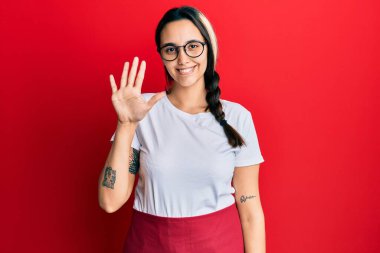 Genç İspanyol kadın profesyonel garson önlüğü giyiyor. Beş numarayı gösterip işaret ediyor. Kendine güvenen ve mutlu bir şekilde gülümsüyor.. 