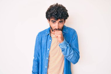 Kıvırcık saçlı ve ayı gibi sıradan kot ceket giyen yakışıklı genç adam kendini iyi hissetmiyor ve soğuk algınlığı veya bronşitin belirtisi olarak öksürüyor. sağlık hizmeti kavramı. 