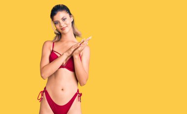 Genç, güzel bir kadın bikini giyiyor, alkışlıyor, mutlu, neşeli ve gururlu elleri alkışlıyor. 