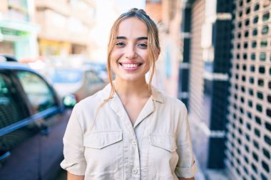 Genç, güzel, sarışın, beyaz bir kadın güneşli bir günde mutlu bir şekilde gülümsüyor.