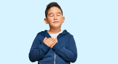 Sıradan spor ceket giyen, elleri göğsünde, gözleri kapalı gülümseyen ve yüzünde minnet ifadesi olan küçük İspanyol çocuk. sağlık kavramı. 