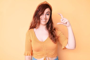 Gündelik kıyafetler giyen, gülümseyen, kendine güvenen, el hareketleriyle küçük beden işareti yapan, parmaklarını gösterip kameraya bakan genç ve güzel bir kadın. ölçüm kavramı. 