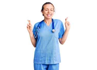 Doktor üniforması giyen ve steteskop işareti yapan genç, güzel sarışın kadın umut ve gözler kapalı bir şekilde gülümsedi. Şans ve batıl inançlar. 