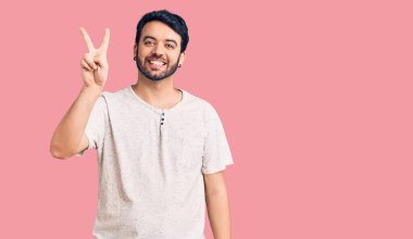 Gündelik kıyafetler giyen genç İspanyol adam iki numarayı gösterip işaret ederken kendinden emin ve mutlu bir şekilde gülümsüyor.. 