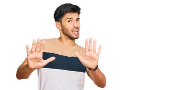 Sıradan kıyafetler giyen genç yakışıklı adam korku ifadesinden korkmuş ve dehşete düşmüş. El hareketlerini durdur, şok içinde bağır. panik konsepti. 