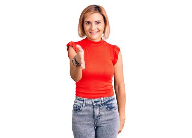 Sıradan kıyafetler giyen genç sarışın kadın gülümseyerek selamlama ve hoş geldin demek için tokalaşmayı teklif ediyor. başarılı iş. 