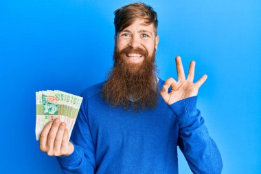 Genç İrlandalı kızıl adam Hong Kong 'u tutuyor. 50 dolarlık banknotlar. Tamam işareti yapıyor. 