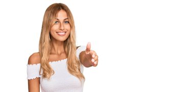 Güzel sarışın genç bayan, günlük beyaz tişört giyip gülümseyerek dostça tokalaşıyor ve hoş geldin diyor. başarılı iş. 