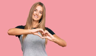 Sıradan kıyafetler giyen, aşık gülümseyen, elleriyle kalp sembolü yapan genç sarışın kadın. romantik kavram. 