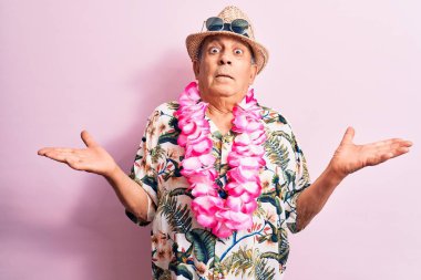 Tatilde olan yakışıklı, kır saçlı, yaz tatili giymiş Hawaii çiçekleri giymiş, kolları açık, kafası karışmış, hiçbir fikri olmayan, kuşkulu bir yüzü olan bir adam..