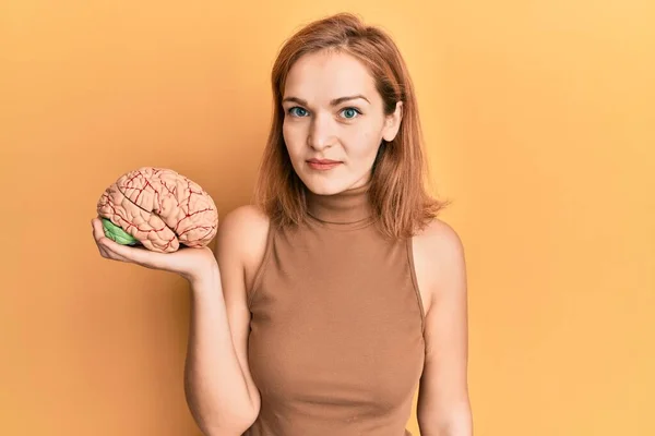 Young caucasian woman holding brain thinking attitude and sober expression looking self confident