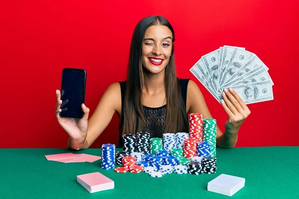 Young Hispanic Woman Playing Poker Holding Smartphone Dollars Winking Looking — Stock Photo, Image