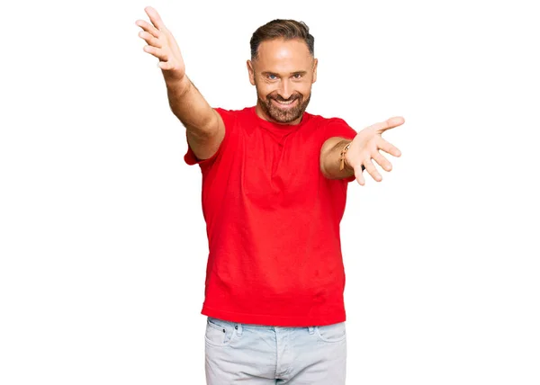 抱擁のために開いた腕で笑顔カメラを見てカジュアルな赤いTシャツを着てハンサムな中年の男 幸せを受け入れる陽気な表情 — ストック写真