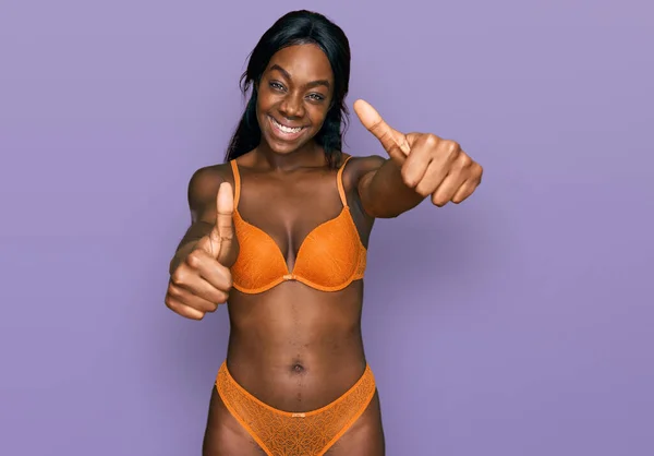 身穿女士内衣的年轻的非洲裔美国女人 赞成用手做积极的手势 微笑着竖起大拇指 为成功感到高兴 优胜手势 — 图库照片