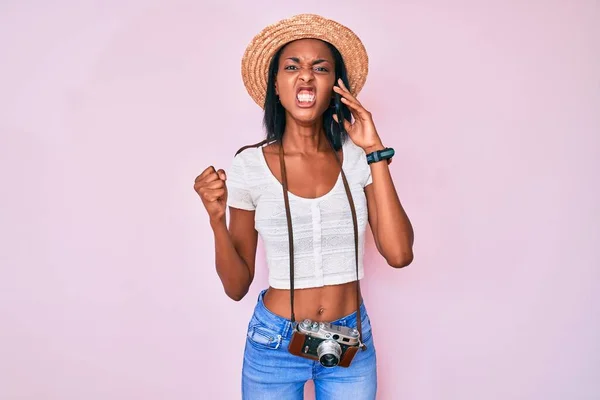 Young African American Woman Holding Vintage Camera Talking Smartphone Annoyed —  Fotos de Stock