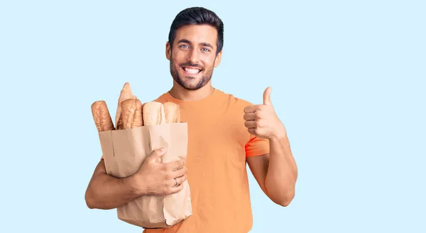 Jonge Spaanse Man Met Papieren Zak Met Brood Glimlachend Gelukkig — Stockfoto