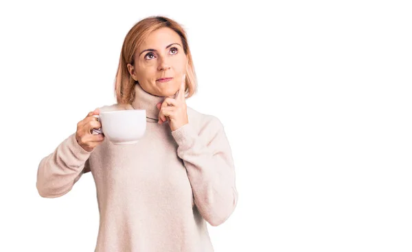Young Blonde Woman Holding Coffee Serious Face Thinking Question Hand — Stock Photo, Image