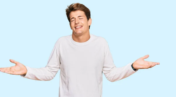 両手を開いてヤシの木を示す プレゼンテーションと広告の比較とバランスを笑顔カジュアルな白いセーターを着てハンサムな白人男性 — ストック写真