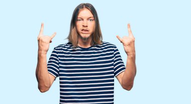 Uzun saçlı, sıradan çizgili tişört giyen, çılgın bir ifadeyle bağıran yakışıklı beyaz adam elleri havada rock sembolü yapıyor. Müzik yıldızı. ağır kavram. 