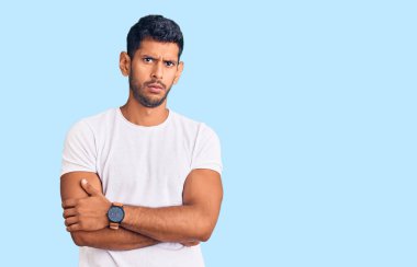 Gündelik kıyafetler giyen genç latin adam şüpheci ve gergin, yüzünde çapraz kollu tasvip etmeyen ifade. negatif kişi. 