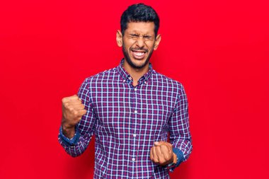 Gündelik giysiler giyen genç Latin adam şaşkınlık ve şaşkınlık içinde başarıyı kollarını kaldırarak ve gözlerini kapatarak kutluyor. 