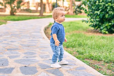 Sevimli ve mutlu küçük çocuk güneşli bir günde parkta eğleniyor. Güzel sarı saçlı erkek çocuk dışarıda oynuyor.