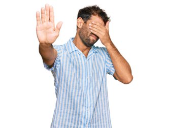 Sakallı yakışıklı genç adam, günlük temiz gömlekler giyiyor, gözleri elleriyle kapatıyor ve üzgün ve korku dolu ifadelerle jestler yapıyor. utangaç ve olumsuz kavram. 