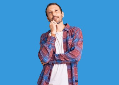 Elleri çenesinde gündelik giysiler giymiş soru soran, düşünceli bir genç adam. Gülümseyen ve düşünceli bir yüz. şüphe kavramı. 