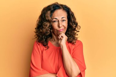 Orta yaşlı İspanyol bir kadın günlük kıyafetler giyip kollarını kavuşturarak depresyondan sıkılmış ve yorgun görünüyor.. 