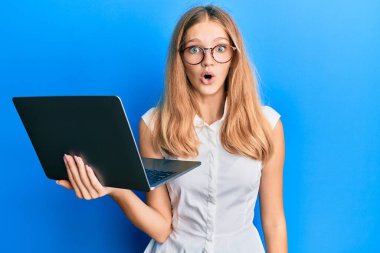 Güzel, genç, beyaz bir kız bilgisayar laptopu kullanıyor. Şaşırtıcı bir şekilde korkmuş ve hayrete düşmüş. İnanmayan yüz. 