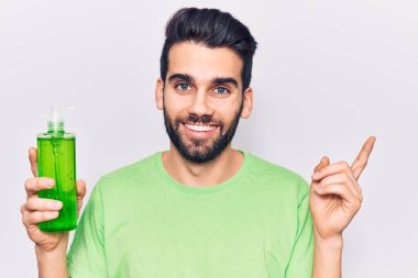 Sakallı genç yakışıklı adam aloe vera kremi şişesi giyiyor gülümsüyor. 