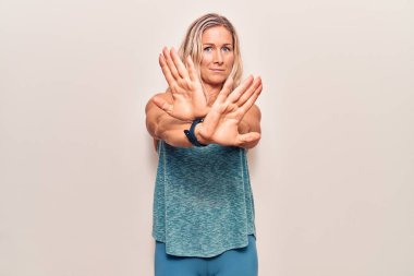 Middle age caucasian blonde woman wearing sportswear rejection expression crossing arms doing negative sign, angry face 