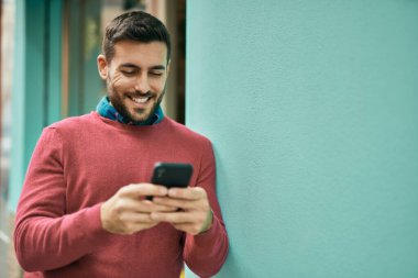 Genç İspanyol adam şehirde akıllı telefon kullanarak mutlu gülümsüyor..