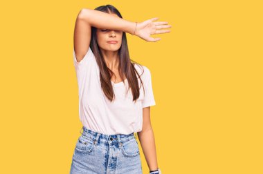 Genç İspanyol kadın sıradan beyaz tişörtler giyip gözlerini kollarıyla kapatıyor, ciddi ve üzgün görünüyor. Görme, saklama ve reddetme konsepti 