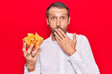 Elinde patates cipsi tutan genç ve yakışıklı bir adam, ağzı ağızla kaplanmış, şok olmuş ve hata yapmaktan korkan. şaşırmış ifade 