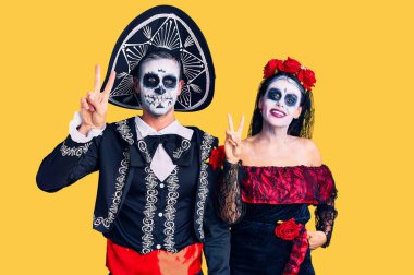 Arka planda Meksika kostümlü genç bir çift gülümsüyor ve parmaklarını zafer işareti yaparken kameraya bakıyor. İki numara.. 