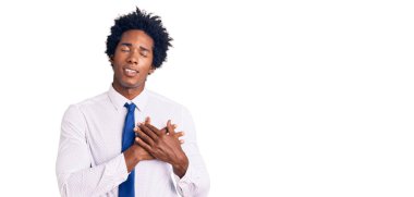 Afro saçlı, iş kıyafetleri giymiş, göğsünde elleri kapalı, yüzünde minnet ifadesi olan yakışıklı Afro-Amerikan bir adam. sağlık kavramı. 