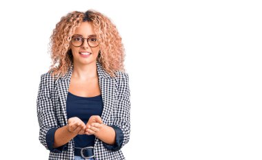 Kıvırcık saçlı, iş ceketi giyen ve elleri avuçlarında gülümseyen, el hareketi yapan genç sarışın kadın. Bekleme ve koruma 