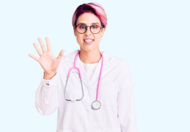 Pembe saçlı, doktor üniforması giyen genç ve güzel bir kadın beş numarayı gösterip işaret ederken kendinden emin ve mutlu bir şekilde gülümsüyor.. 