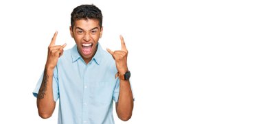 Genç, yakışıklı, Afro-Amerikalı, günlük kıyafetler giymiş, çılgın bir ifadeyle bağırıyor, elleri havada rock sembolü yapıyor. Müzik yıldızı. ağır müzik konsepti. 