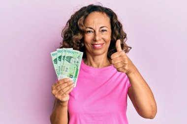 Orta yaşlı İspanyol kadın elinde 10000 Güney Koreli ile mutlu ve olumlu gülümseyen, başparmağını kaldıran ve onay işareti yapan banknotlar kazandı. 