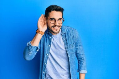 Gündelik giysiler ve gözlük takan genç İspanyol adam kulağına fısıldayarak dedikodu ve dedikoduları dinliyor ve dinliyor. Sağırlık kavramı. 