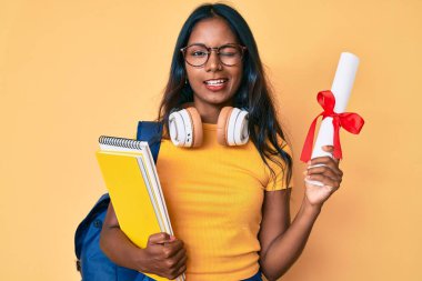 Sırt çantalı genç Hintli kız. Elinde diplomayla kameraya bakıyor. Seksi bir ifadeyle, neşeli ve mutlu bir yüzle.. 